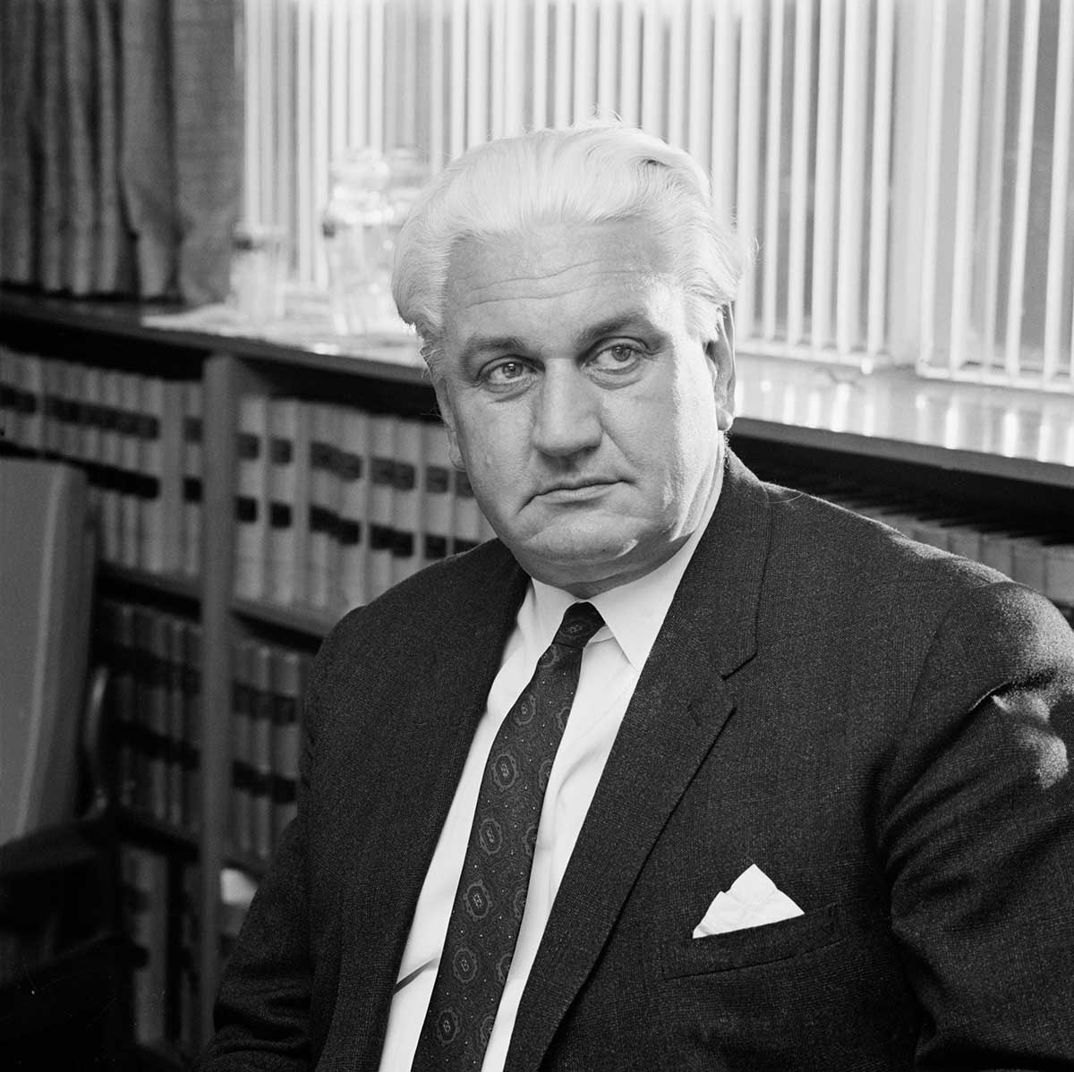 Black and white portrait photograph of a suited man in an office.