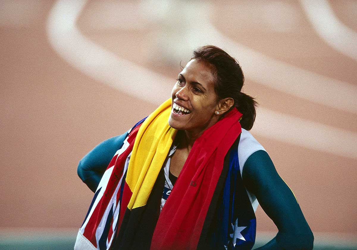 Cathy Freeman on the race track draped in the Australian and Aboriginal flags.