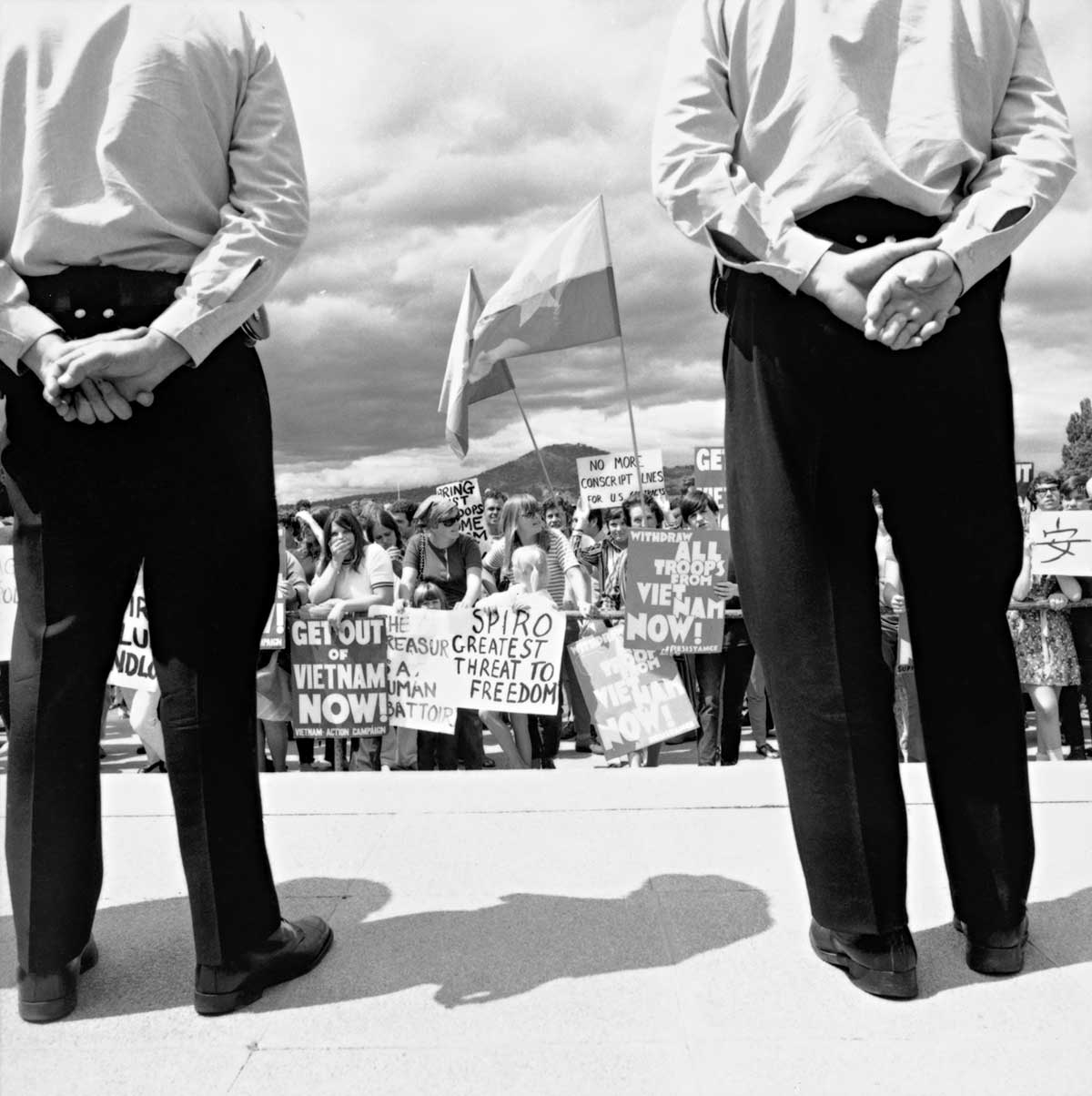 Black and white photograph of two police standing calmly while surveying a large group of protesters.