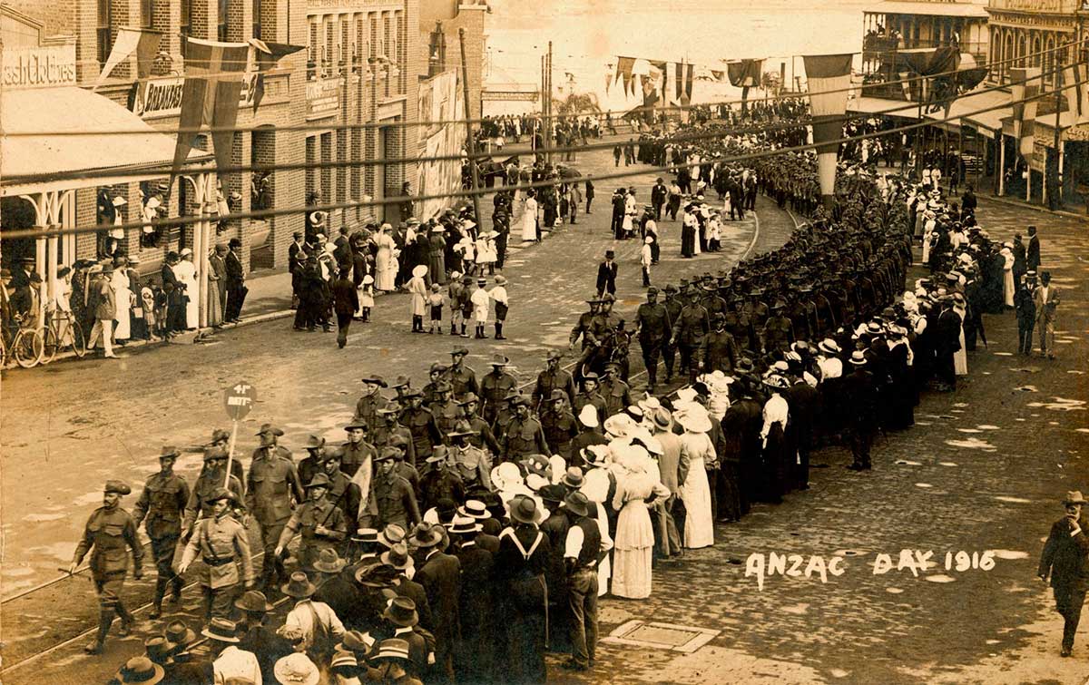 Black and white photograph of large crowds gathered in a city street to watch a parade of Australian and New Zealand soldiers. Printed in the bottom right corner is 'ANZAC DAY 1916'.