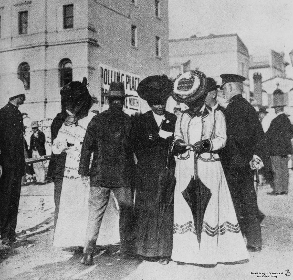 Two women in period clothing standing in a street amongst other people. They are looking at small slips of paper.