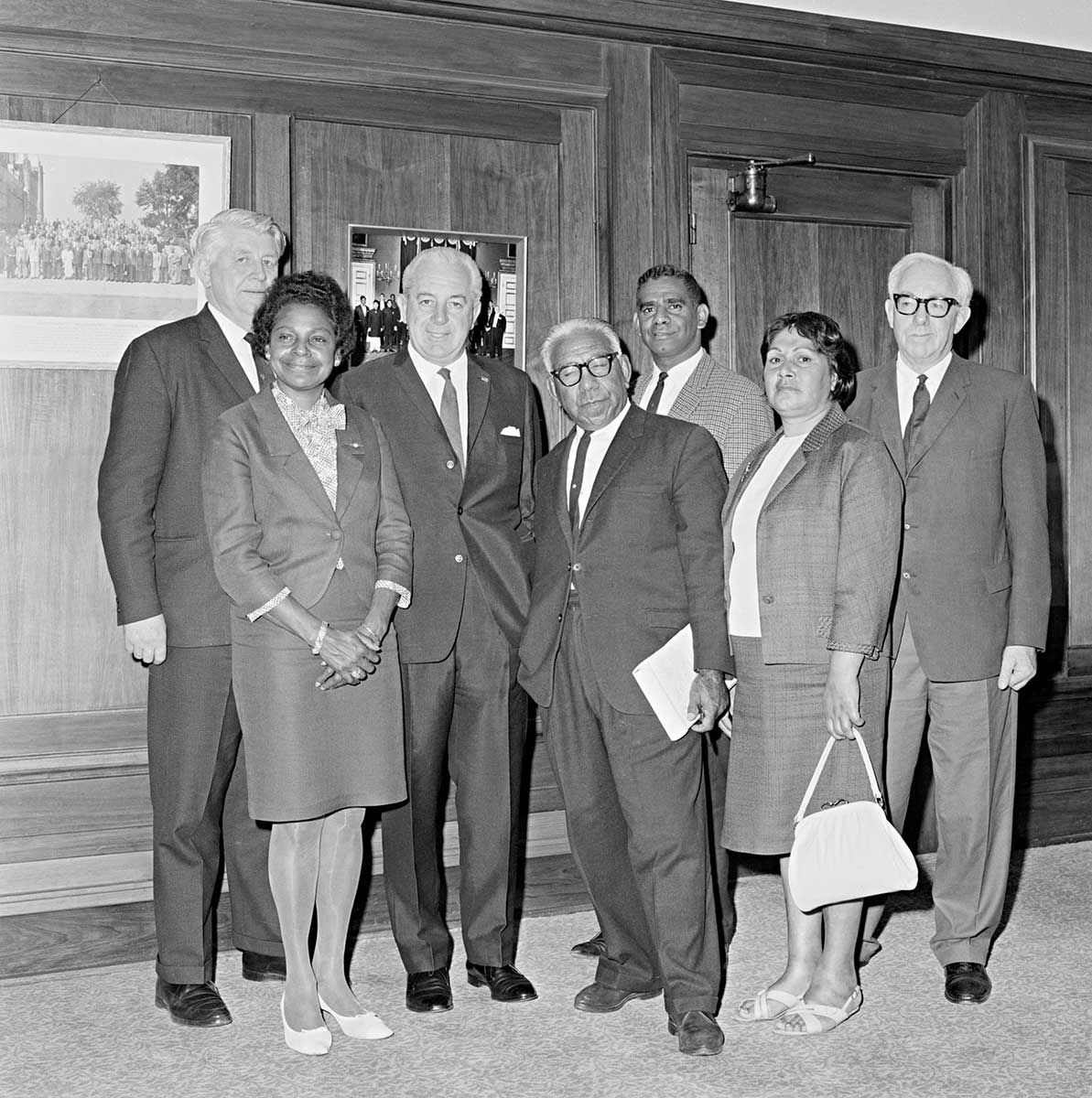 The seven people named stand in front of a wood-panelled wall in what looks like Old Parliament House.