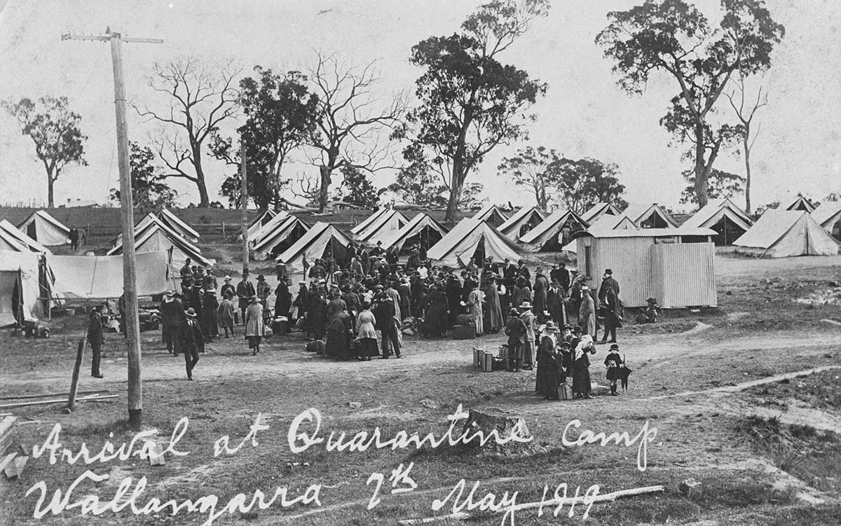 Black-and-white photograph of a crowd of people gathered in a camp site. Hand written at the bottom is "Arrival at quarantine camp. Wallangarra 7th May 1919".
