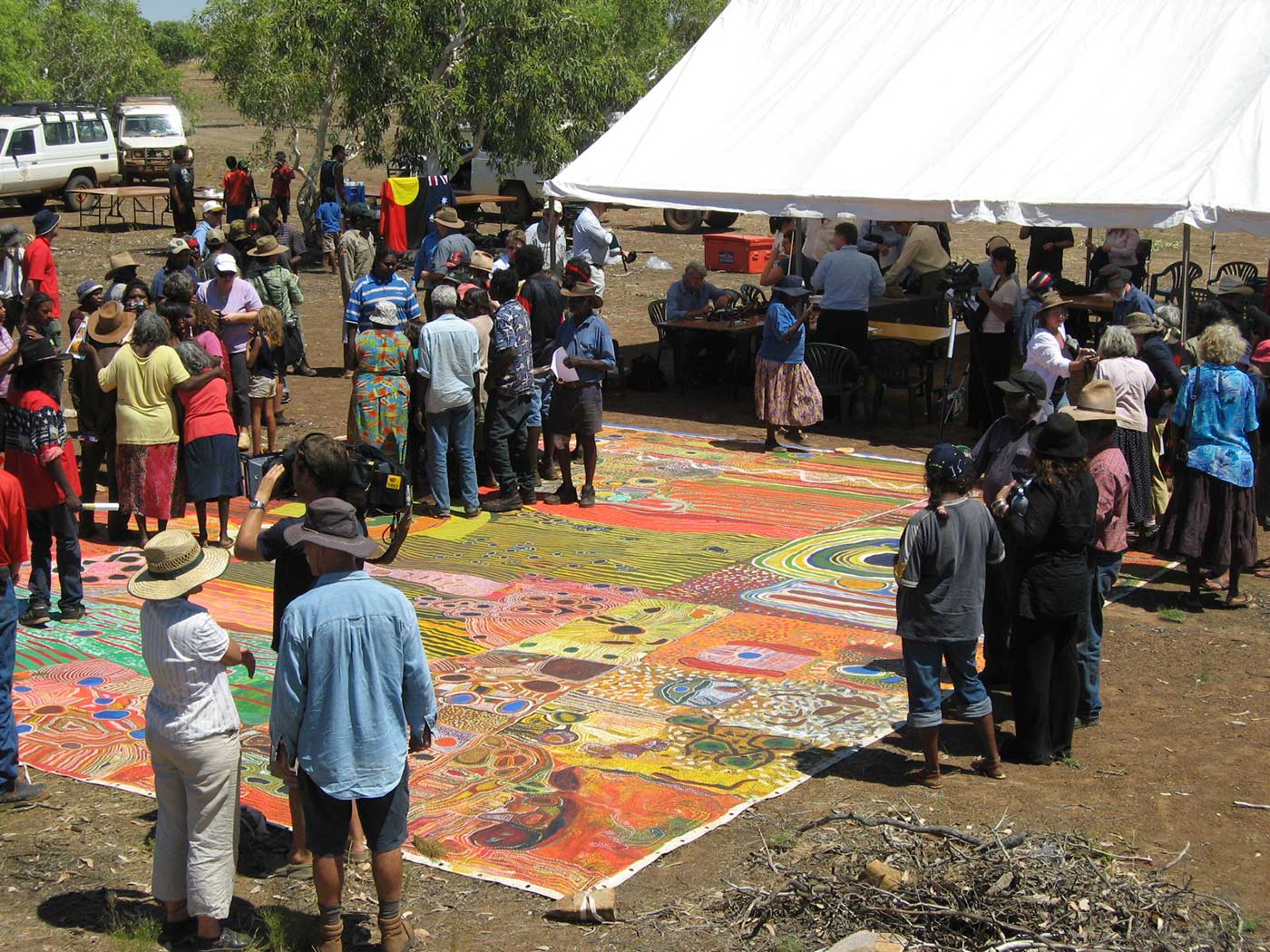 A whole group of people standing around a large canvas, outside.