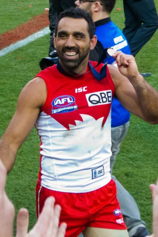 Photograph of a smiling man, holding up a sporting medal.