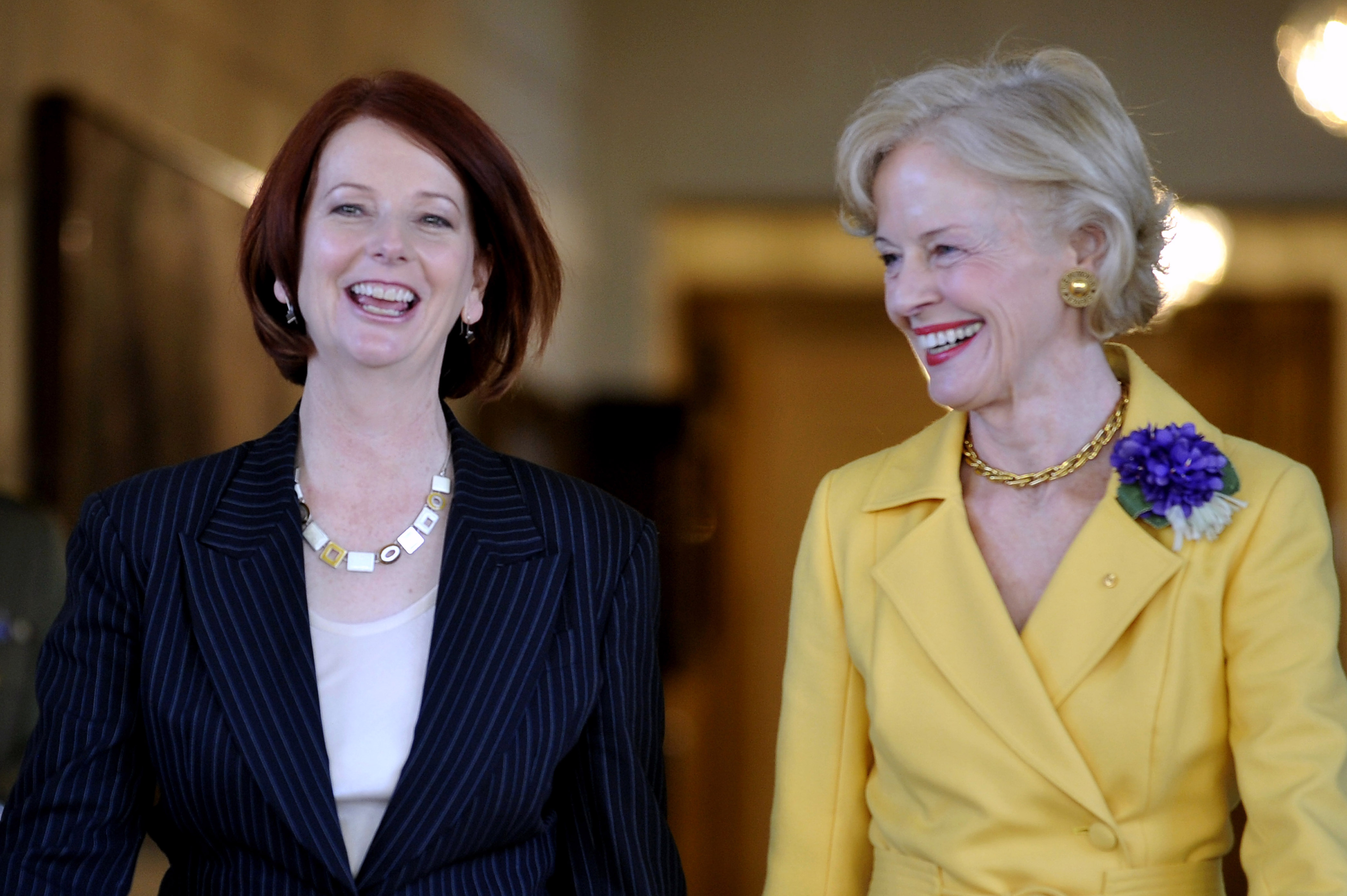 Photograph of Julia Gillard and Quentin Bryce. Julia is wearing a black jacket, white top and necklace. Quentin is wearing a yellow jacket with large purple flower on the collar.