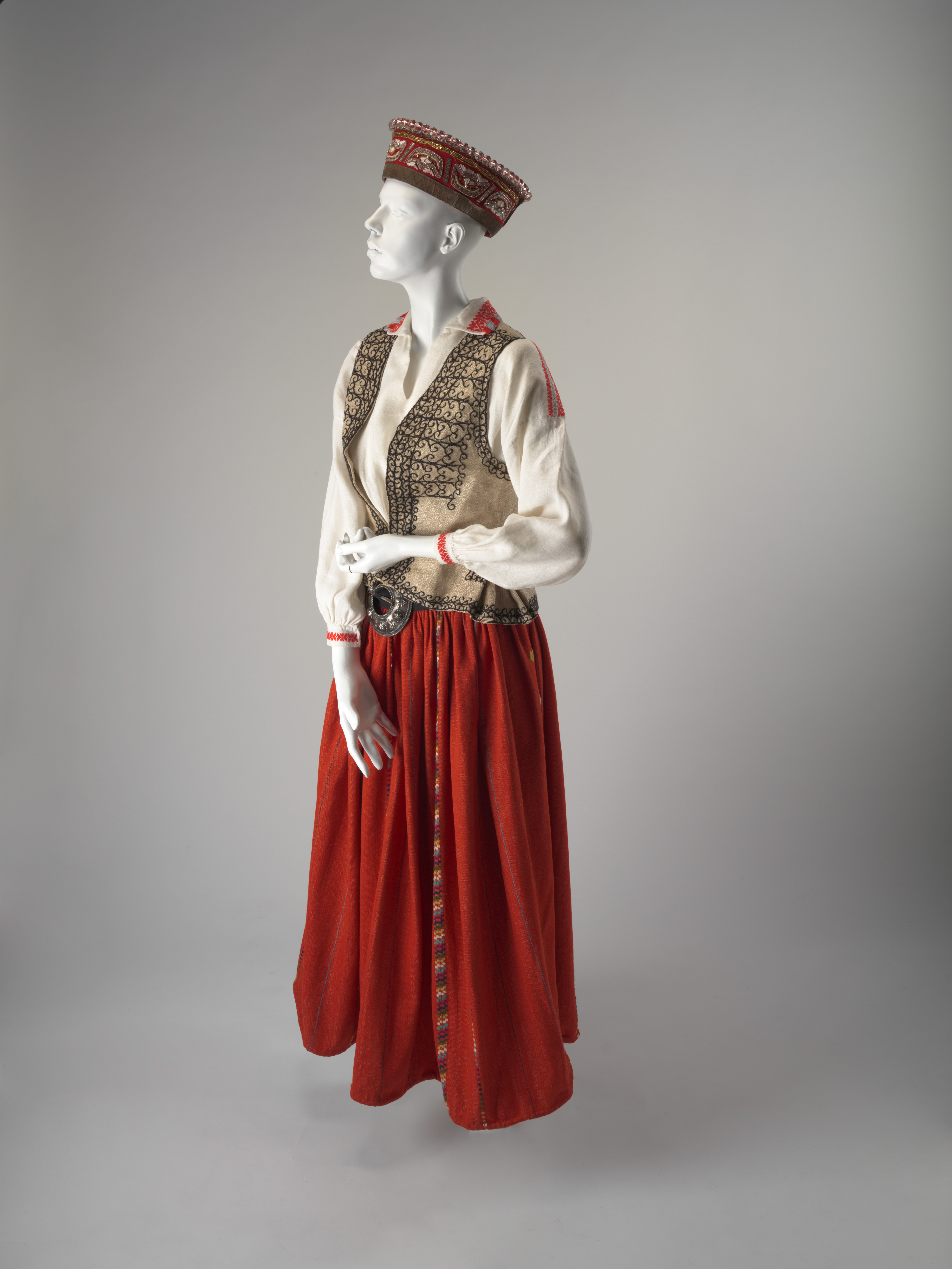 A white linen shift blouse decorated with embroidered geometric patterns in red and grey at the collar, the cuffs and the shoulders.