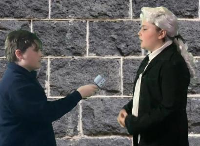 A child holding a microphone and interviewing a version of himself dressed in a suit and white wig.