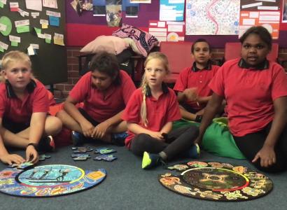 Five school children in uniform sitting on a classroom floor around two puzzles.