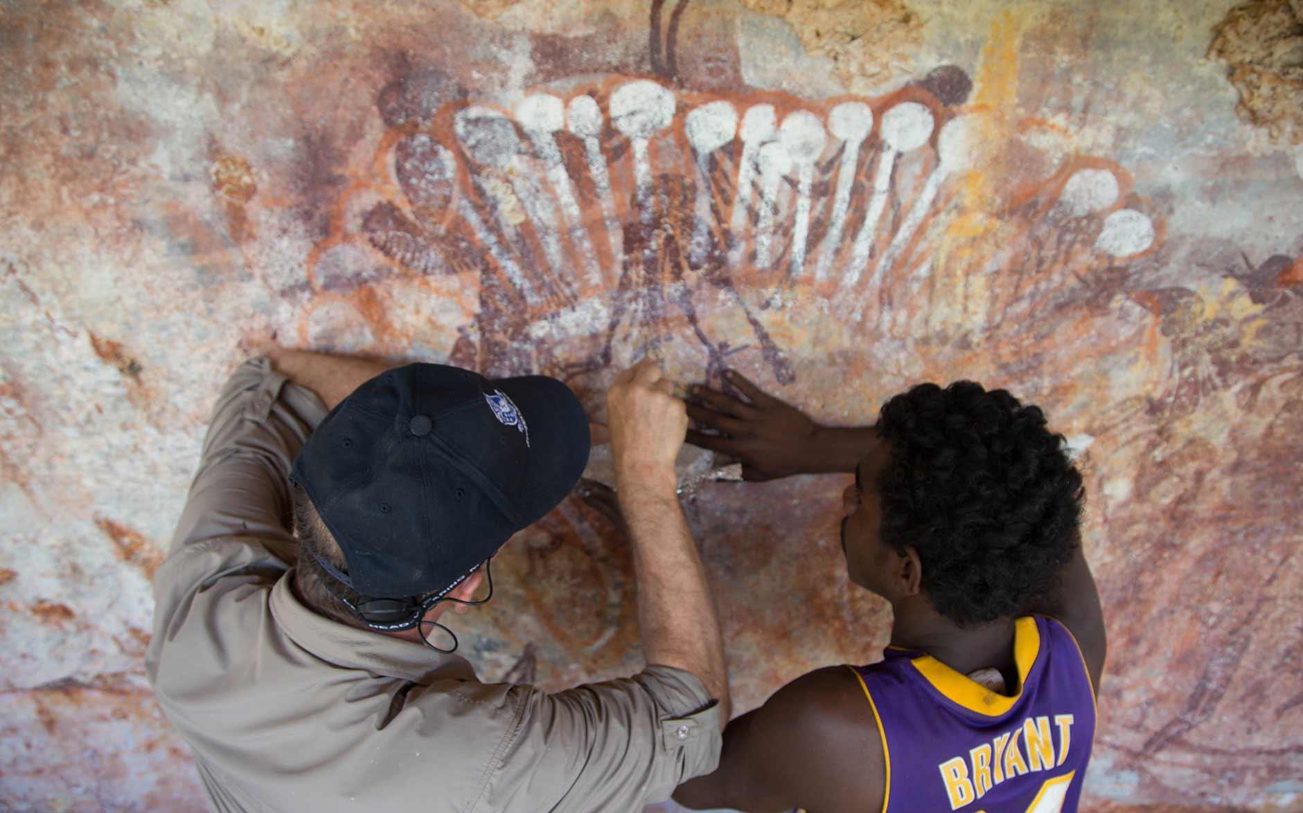Photograph of two men scraping a sample of paint from rock art.